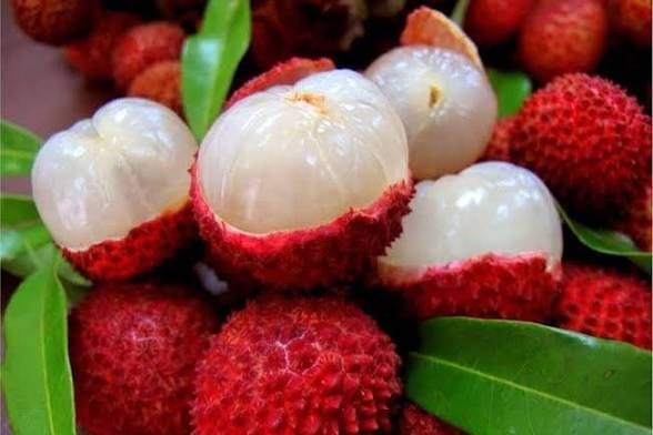 Ripe lychees among green leaves, several part-peeled to show the flesh inside