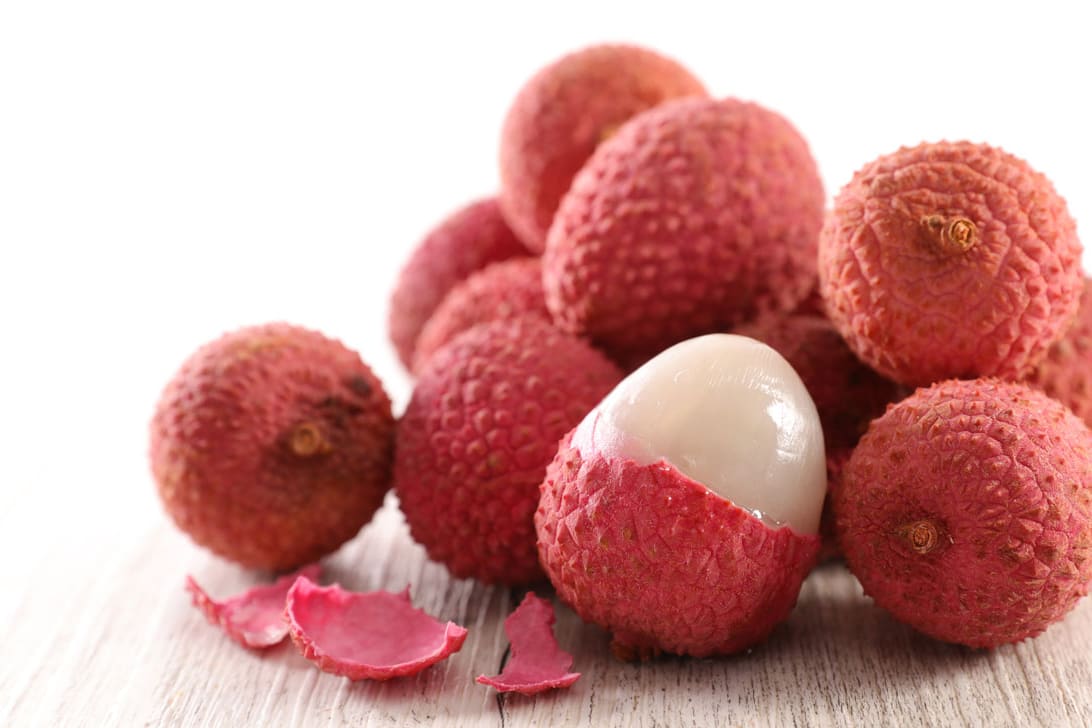 A heap of freshly picked lychees on a wooden surface, one peeled to show the flesh